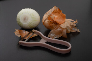Peeled onion and onion peel next to it on black table and vegetable peeling knife.Close up of dry...
