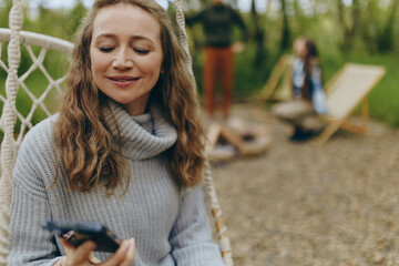 Middle age woman enjoying wellness lifestyle, sitting in hammock outdoors with relaxed smile, embracing active wellbeing and health in natural community setting.
