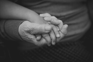 Close-up of elderly and child hands holding each other, expressing warmth, care and generational bond, concept of family and connection black and white photo grandmother and granddaughter