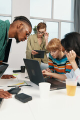 Young adult woman and coworkers working together in a modern workplace, socializing and collaborating on business tasks with laptops and digital devices in a bright office environment.