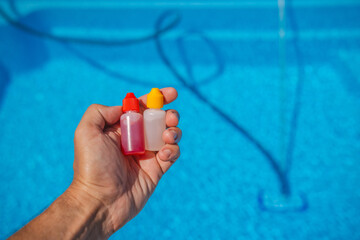 Close-up of a hand holding two dropper bottles with red and yellow caps, used for pool water...