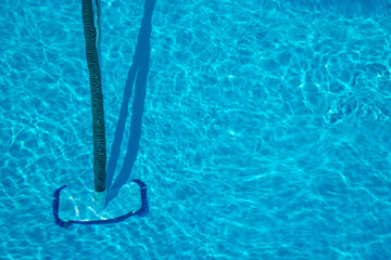 Manual pool vacuum with flexible hose and telescopic pole cleaning the bottom of a clear swimming...