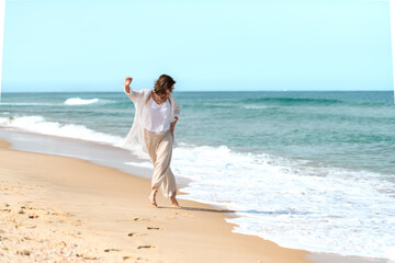 Beautiful mature woman having fun running away from the waves on sandy beach on sunny summer day.