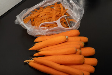 Carrot waste in a bio-bag and peeled carrots on a black table.View of a pile of various organic...