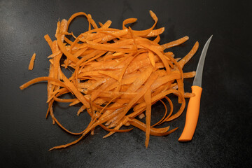 Carrot waste on black table and vegetable peeler.View of pile of various organic waste after...