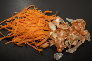 Onion peel and carrot waste on black table and vegetable peeling knife.View of pile of various...