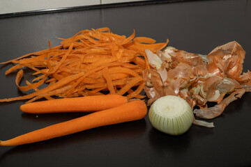 Onion peel and carrot waste on black table and vegetable peeling knife.View of pile of various...