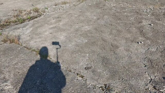 Photographer or vloger shadow walking and taking selfie on cracked concrete ground