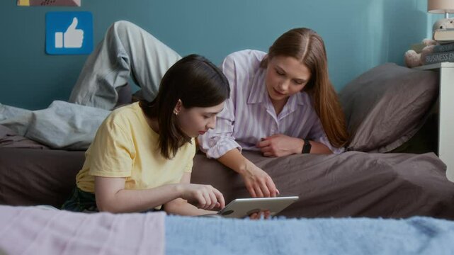 Shot of two girls as roommates in college dorm room together using digital tablet and eating snacks