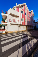 A vibrantly striped red and white building with distinctive balconies and windows stands beside a pedestrian crosswalk