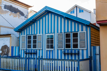 A quaint, blue and white striped wooden house with a white picket fence and shuttered windows