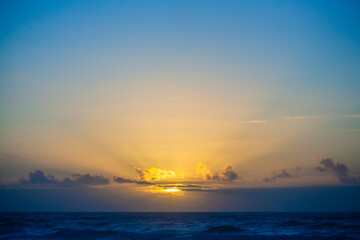 Silhouetted figures stand on a rocky shore at sunrise