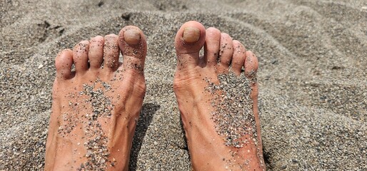 
Close-up of two sandy feet lying on the beach, partially covered with fine grains of sand under...