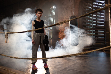 A woman in a boxing gym, portrait by the ropes, cinematic style, dark tones. Training and...
