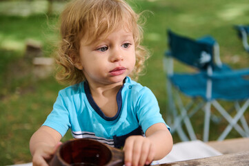 Young Child Sitting Outdoors Enjoying a Beverage at a Sunny Park Picnic