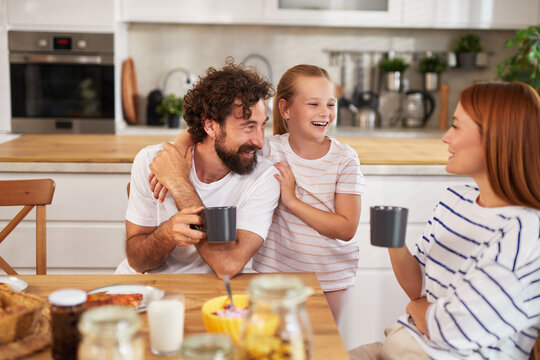 A family breakfast features a father and daughter sharing a lighthearted moment while a mother engages in cheerful conversation, all in a bright kitchen.