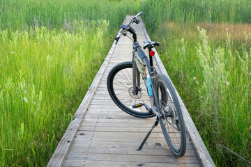 hybrid bike with kickstand, frame bag and cycling computer on a boardwalk across wetland in summer scenery