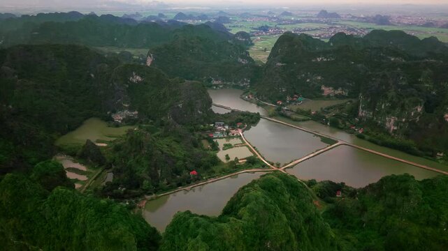 Beautiful drone footage of Hang Mua, Tam Coc in Ninh Binh, Vietnam. Lush green trees surround towering limestone cliffs in this peaceful and beautiful aerial view of rural Vietnam.