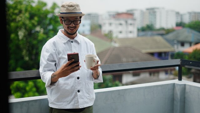 Chef relaxing on balcony, enjoying coffee and browsing smartphone, with cityscape view