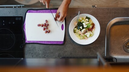 Chef cutting fresh grapes on a white cutting board, preparing a healthy fruit salad in a modern...