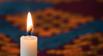 Glowing candle flame illuminating a tranquil scene with an ornate background, radiating warmth and evoking a sense of peace.