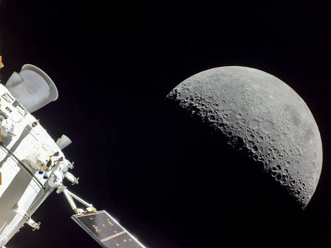 A spacecraft solar panel and module frame a sharply detailed crescent Moon against the blackness of space. Image courtesy of NASA