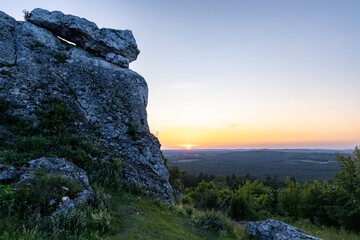Golden Hour View from a Rocky Perch.A breathtaking view of a vibrant sunset casting warm, golden light over a sprawling forested valley.