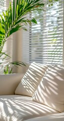 A bright and airy sunroom filled with natural light, featuring white horizontal curtains, lush green palm leaves, and a cozy cream-colored sofa, all bathed in warm golden sunlight.