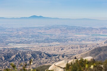 A hiker pauses atop a rock formation to admire the vast valley view in Southern California, USA. The scene captures a moment of reflection and appreciation for nature.