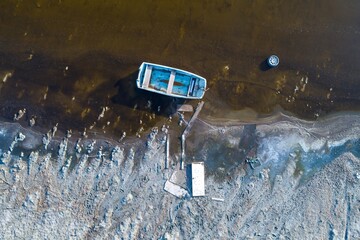 Aerial view of a small boat, tire, and debris on a polluted shoreline, illustrating environmental...