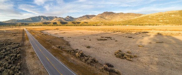 A rural road cuts through a vast, dry landscape in Thomas Mountain, Mountain Center, California, USA, leading towards distant mountains under a clear sky.