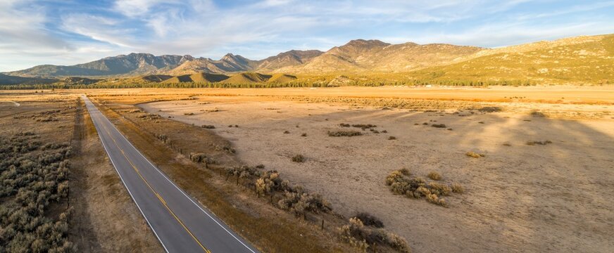 A rural road cuts through a vast, dry landscape in Thomas Mountain, Mountain Center, California, USA, leading towards distant mountains under a clear sky.