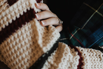 Close-up of hand wearing engagement ring and wedding band with French manicure on striped crocheted...