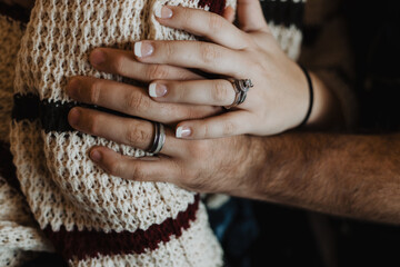 Close-up of female hand with engagement ring and wedding band resting on male hand wearing wedding...