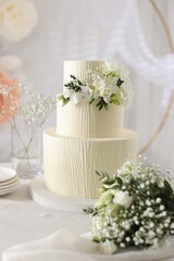 Delicious wedding cake with floral decor and bouquet on table indoors