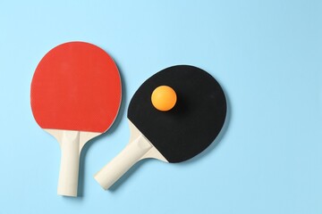 Ping pong rackets and ball on light blue background, flat lay. Space for text
