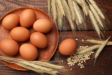 Raw eggs and spikes of wheat on wooden table, flat lay