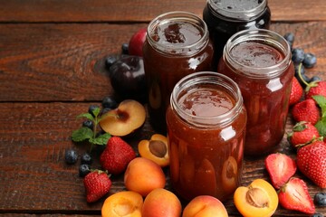 Different jams in jars and ingredients on wooden table, closeup