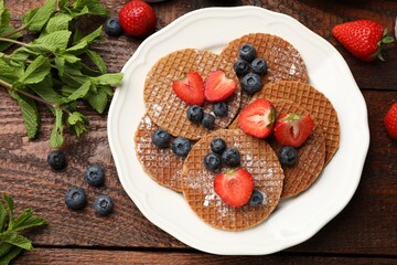 Tasty Dutch waffles (stroopwafels), mint and berries on wooden table, flat lay