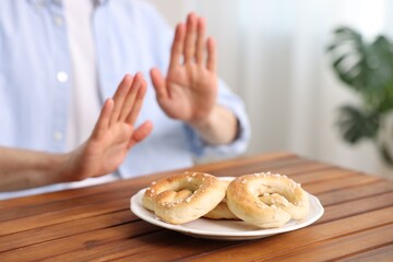 Gluten free diet. Man refusing from pretzels at wooden table indoors, selective focus