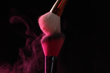 Makeup brushes with pink eye shadow on black background, closeup