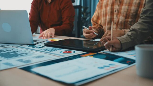 A group of business professionals collaborates in a modern office, analyzing financial data on charts and tablets, focused on strategy and insights for better decision-making. SACTR