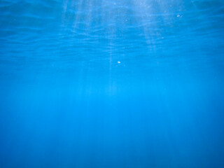 Dark blue ocean surface seen from underwater. Abstract waves underwater and rays of sunlight...