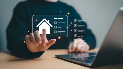 Fototapeta premium Person s hand interacting with a digital interface displaying a house icon and a checklist with completed tasks next to a laptop