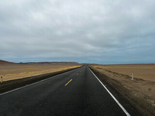 Straight paved road going through desert landscape in National Park Reserve Paracas in Pisco Province, Peru. Popular tourist route offers access to various viewpoints and beaches.