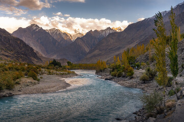 Dramatic Mountain Range with Autumn Trees and River Flowing Through Rugged Valley at Sunset