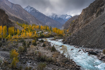A breathtaking view of a serene mountain valley in autumn, featuring a crystal-clear river winding...