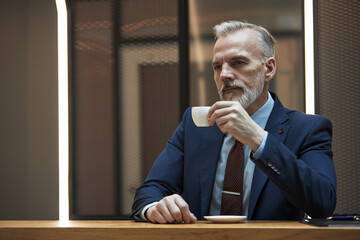 Portrait of senior businessman wearing formal attire holding coffee cup while contemplating....