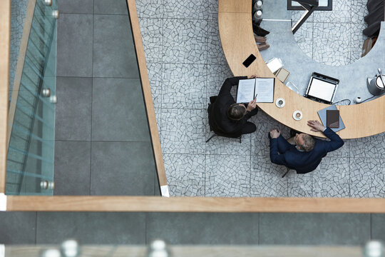 Overhead perspective of professionals engaging in meeting around modern conference table with document and tablet visible on table, cups of coffee