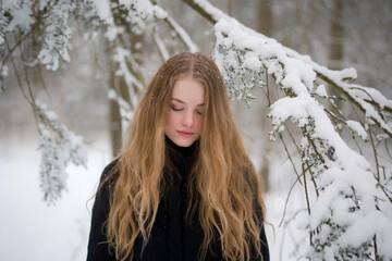 A winter portrait photograph of a young woman with long, wavy honey-blonde hair wearing a black turtleneck sweater. 